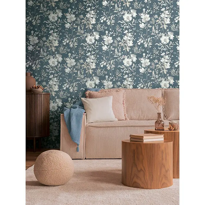 A.S. Création Cosmoliving by Cosmopolitan Vliestapete Blüten - Blau-Metallic-Weiß, Floral, 10,05 x 0,53 m - Einrichtungsszene mit einer blumengemusterten Tapete in Blau- und Grautönen hinter einem rosa Cord Sofa und Holzelementen.