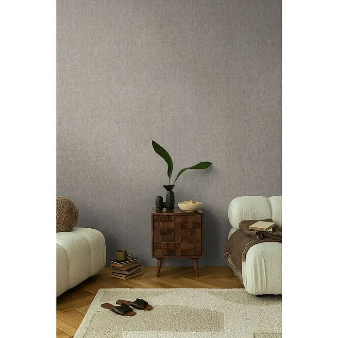 A.S. Création Cosmoliving by Cosmopolitan Vliestapete - Grau, Uni, 10,05 x 0,53 m - Wohnzimmer-Szene mit einem Nachttisch aus Holz mit Dekor, einem cremefarbenen Sofa und einem hellen Teppich auf einem Holzboden.