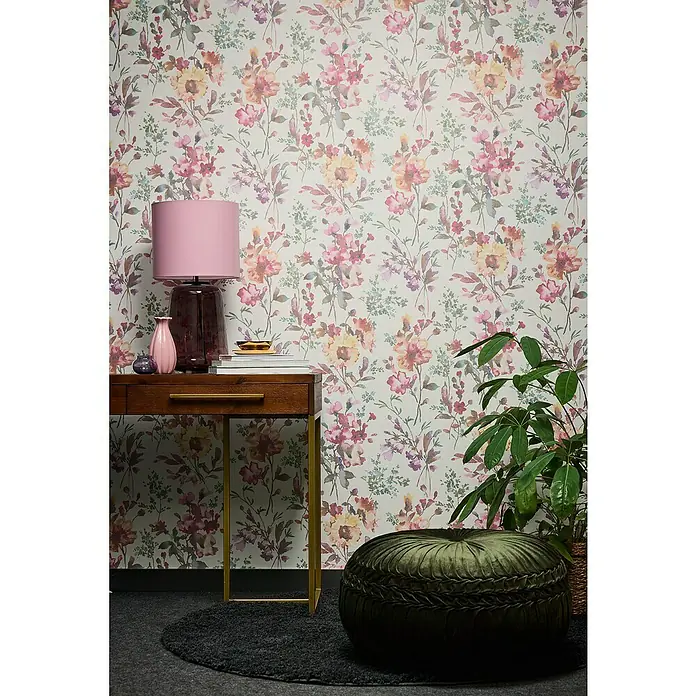 A.S. Création Cosmoliving by Cosmopolitan Vliestapete Blüten - Weiß-Metallic-Grün, Floral, 10,05 x 0,53 m - Detailaufnahme eines Raumes mit blumiger Tapete, einem Holztisch mit Lampe und Dekorationen sowie einem grünen Sitzkissen und einer Zimmerpflanze.