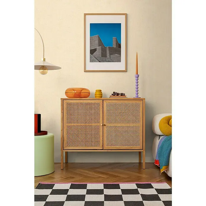 A.S. Création Cosmoliving by Cosmopolitan Vliestapete - Beige II, Uni, 10,05 x 0,53 m - Ein stilvolles Sideboard aus hellem Holz mit Rattanfronten unter einem gerahmten Bild und dekorativen Objekten.