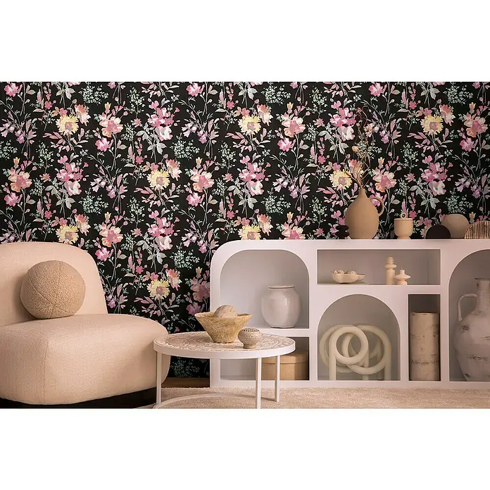 A.S. Création Cosmoliving by Cosmopolitan Vliestapete Blüten - Schwarz-Pink-Grün, Floral, 10,05 x 0,53 m - Zimmer mit schwarzer Blumtapete, beigem Sessel, weißem Tisch und Regal mit Dekorationen.