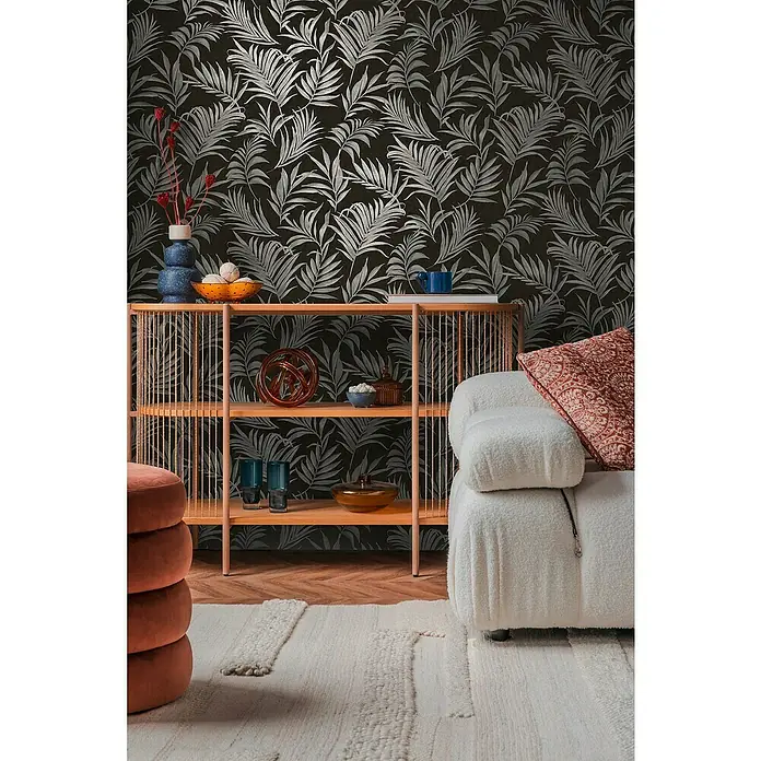 A.S. Création Cosmoliving by Cosmopolitan Vliestapete Ranken - Schwarz-Grau-Blau, Floral, 10,05 x 0,53 m - Detailaufnahme eines Wohnzimmers mit einer Konsole, Dekorationen und einem weißen Sessel vor einer Tapete mit tropischen Pflanzenmotiven.
