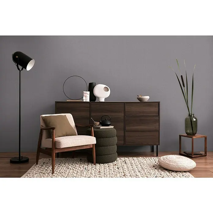 A.S. Création Cosmoliving by Cosmopolitan Vliestapete - Dunkelgrau, Uni, 10,05 x 0,53 m - Interieur mit dunklem Holzschrank, Sessel mit Kissen und einer Stehlampe. Dekorative Elemente wie Vasen und ein Hocker ergänzen das Arrangement.
