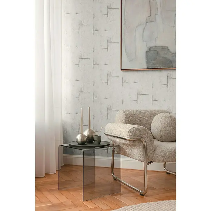 A.S. Création Cosmoliving by Cosmopolitan Vliestapete Beton - Grau-Weiß, Betonoptik, 10,05 x 0,53 m - Nahaufnahme eines modernen Wohnzimmers mit einem Glasbeistelltisch, Kerzenständern und einem Bouclé-Sessel, dekoriert mit einem abstrakten Gemälde.