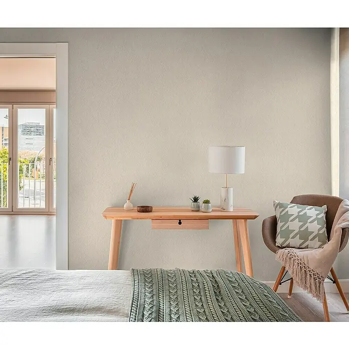 A.S. Création Hygge 3 Vliestapete - Beigebraun, Uni, 10,05 x 0,53 m - Gemütliches Schlafzimmer mit Holztisch, Lampe und Stuhl mit Kissen. Das Zimmer strahlt eine behagliche Atmosphäre aus.