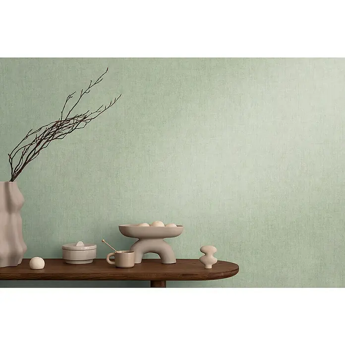 A.S. Création Cosmoliving by Cosmopolitan Vliestapete - Hellgrün, Uni, 10,05 x 0,53 m - Stilleben mit einer Vase, Ästen, einer Schale mit Kugeln, einer Tasse und einer Dose auf einem Holztisch vor einer hellgrünen Wand.