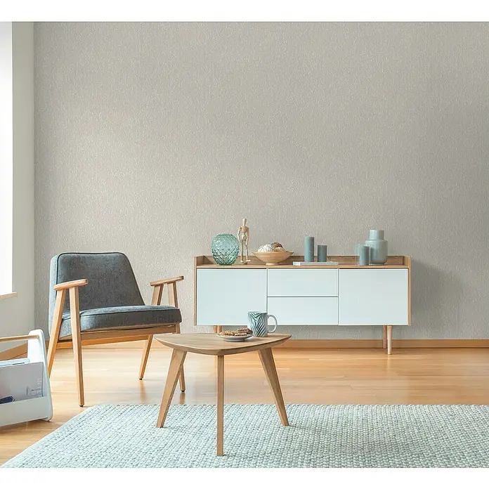 A.S. Création Hygge 3 Vliestapete Ranken - Grau-Creme, Floral, 10,05 x 0,53 m - Wohnzimmer mit einem grauen Sessel, einem Couchtisch und einem weißen Sideboard dekoriert mit Vasen und Kerzen.