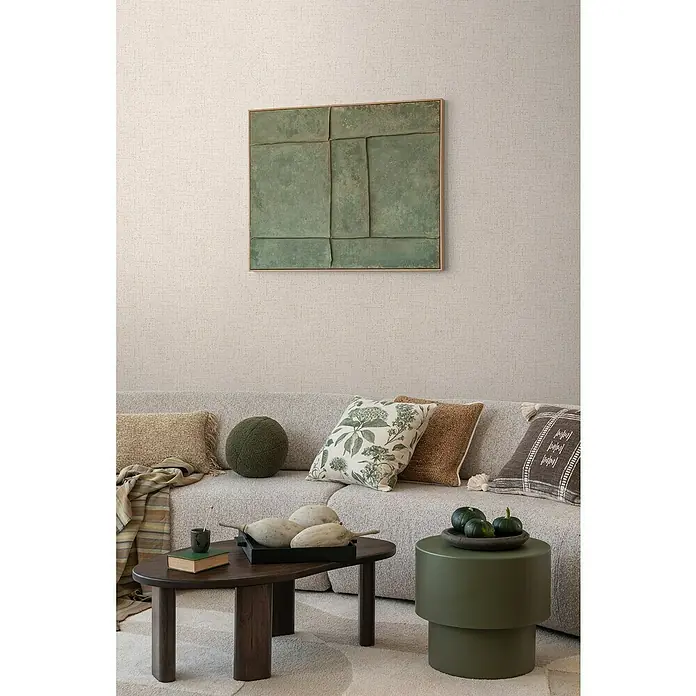 A.S. Création Cosmoliving by Cosmopolitan Vliestapete - Cremegrau, Uni, 10,05 x 0,53 m - Wohnzimmerdekoration mit einem stilvollen Sofa, Kissen und einem dunklen Holztisch mit Deko, ergänzt durch ein grünes Kunstwerk an der Wand.