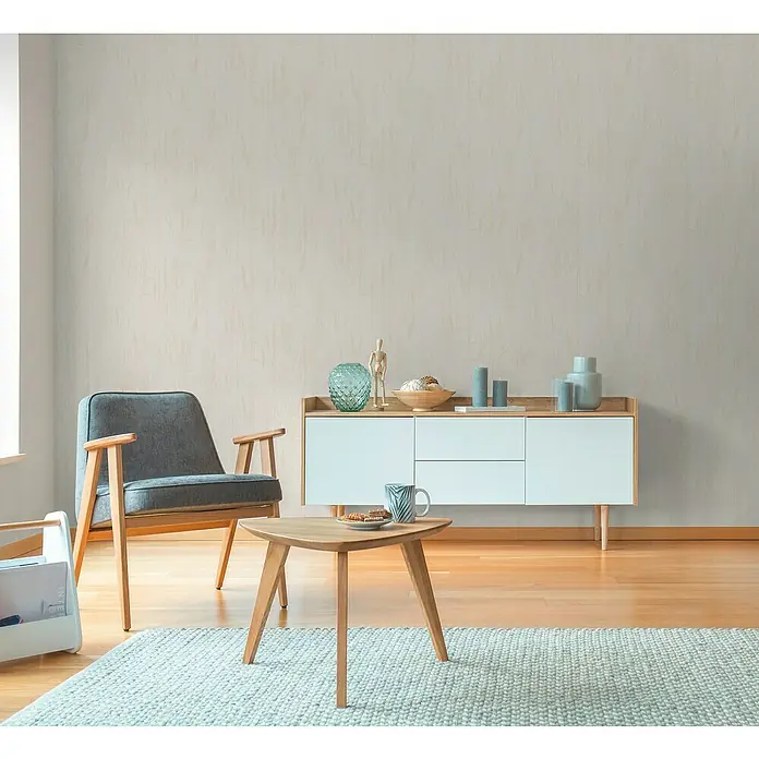 A.S. Création Hygge 3 Vliestapete Floral - Beige-Creme, Floral, 10,05 x 0,53 m - Elegantes Wohnzimmer-Interieur mit einem grauen Sessel, einem weißen Sideboard und einem dreieckigen Couchtisch auf einem hellblauen Teppich.