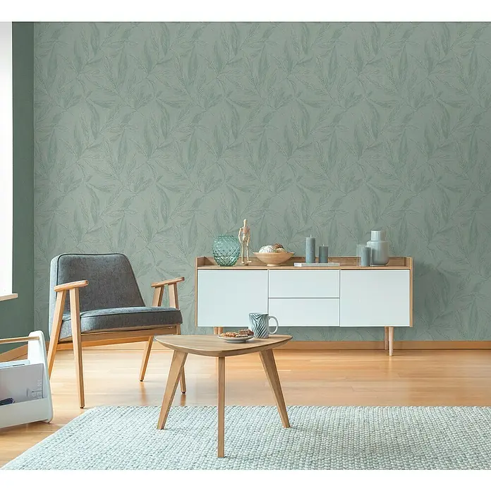 A.S. Création Hygge 3 Vliestapete Blätter - Grün-Metalllic, Floral, 10,05 x 0,53 m - Einladendes Wohnzimmer mit einem modernen grauen Sessel, einem stilvollen Sideboard und einem gemusterten Teppich.