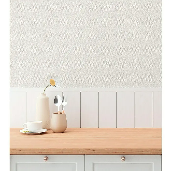 A.S. Création Hygge 3 Vliestapete - Hell-Grau, Uni, 10,05 x 0,53 m - Nahaufnahme eines Küchentisches mit Geschirr, einer Blume und einer Kaffeetasse. Die Arbeitsplatte ist hellbraun und darunter befinden sich Schubladen.