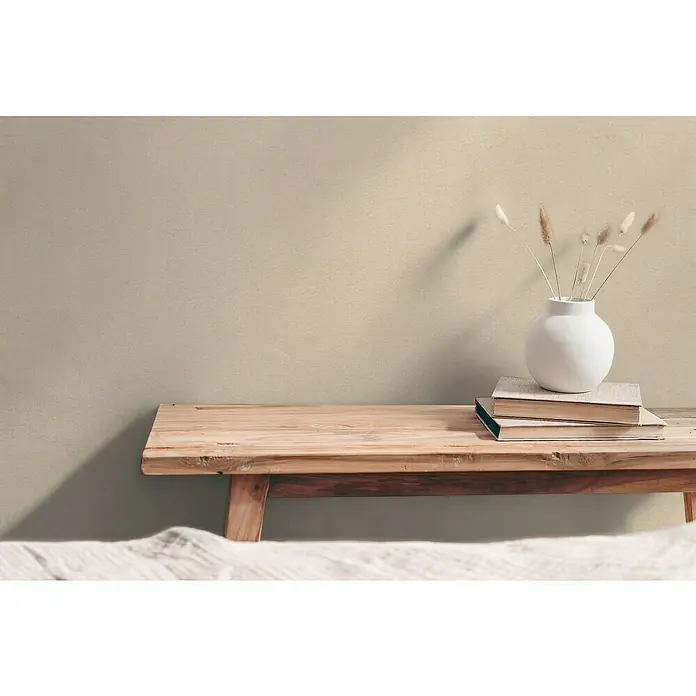 A.S. Création Hygge 3 Vliestapete - Beige, Uni, 10,05 x 0,53 m - Einrichtung mit rustikaler Holzbank, darauf Bücher und eine elegante weiße Vase mit Trockenblumen, die dem Raum eine stilvolle Note verleihen.