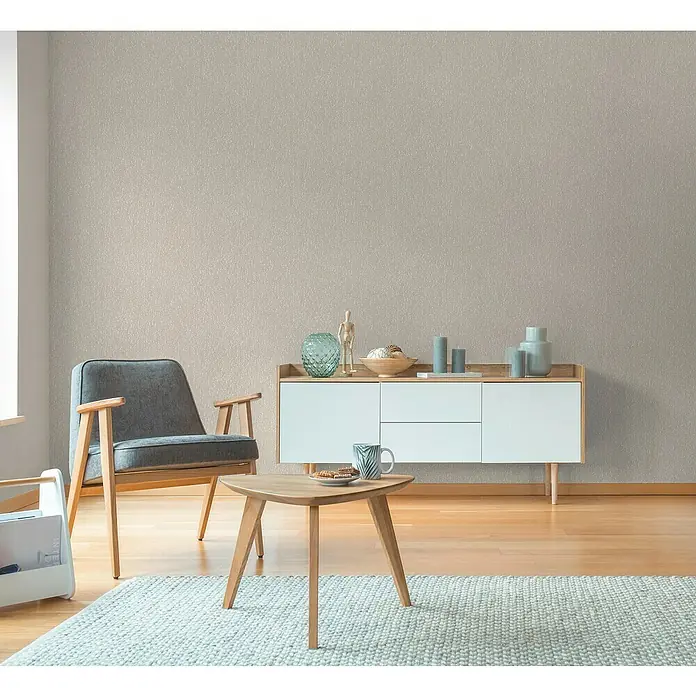 A.S. Création Hygge 3 Vliestapete Ranken - Greige, Floral, 10,05 x 0,53 m - Wohnzimmer-Szene mit einem grauen Sessel, einem weißen Sideboard und einem kleinen Holztisch auf einem hellen Teppich.