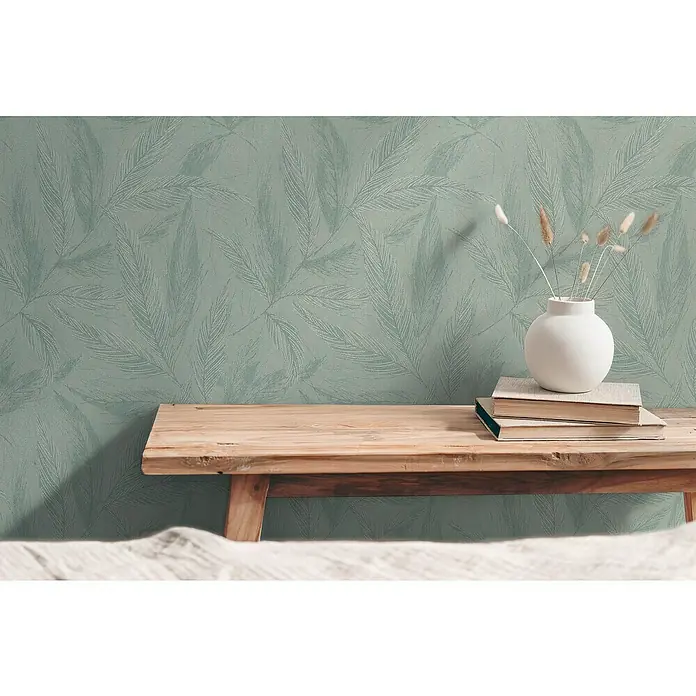 A.S. Création Hygge 3 Vliestapete Blätter - Grün-Metalllic, Floral, 10,05 x 0,53 m - Nahaufnahme eines Holzregals mit Büchern und einer weißen Vase mit Blumen vor einer mintgrünen Blättertapete.