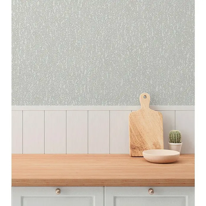 A.S. Création Hygge 3 Vliestapete Ranken - Grau, Floral, 10,05 x 0,53 m - Eine Nahaufnahme einer Küche mit einem Schneidebrett, einer Schüssel und einem Kaktus auf einer hellen Holzplatte. Die Küchenschränke sind in einem hellen Grauton gehalten.