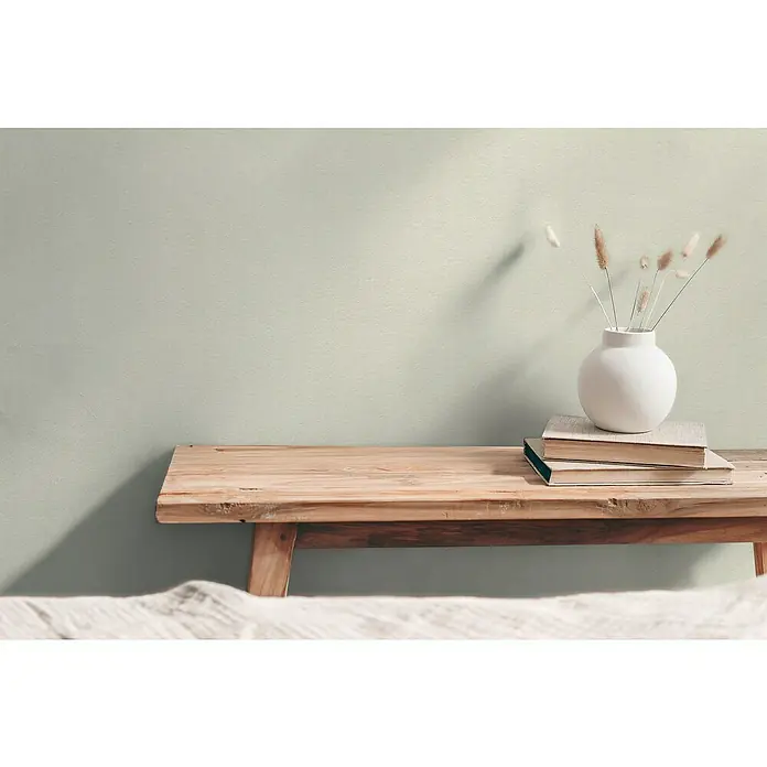 A.S. Création Hygge 3 Vliestapete - Hellgrün, Uni, 10,05 x 0,53 m - Schlichtes Interieur mit einer Holzbank, Büchern und einer Vase mit Trockenblumen vor einer dezenten Wand. Natürliches, ruhiges Ambiente.