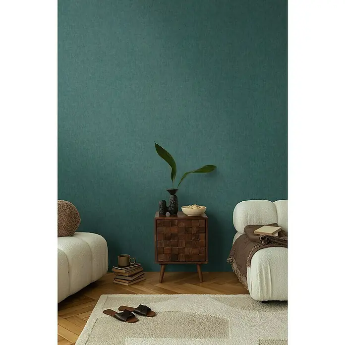 A.S. Création Cosmoliving by Cosmopolitan Vliestapete - Dunkelgrün, Uni, 10,05 x 0,53 m - Ein gemütliches Wohnzimmer mit einem Nachttisch aus Holz, einer Lampe, einem Buch und einer Couch.