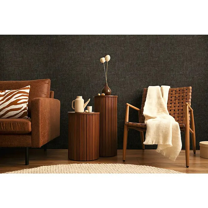 A.S. Création Cosmoliving by Cosmopolitan Vliestapete - Schwarz, Uni, 10,05 x 0,53 m - Einladende Wohnzimmerszene mit braunem Ledersofa, gewebtem Sessel und stilvollen Beistelltischen aus Holz in einem gemütlichen Ambiente.