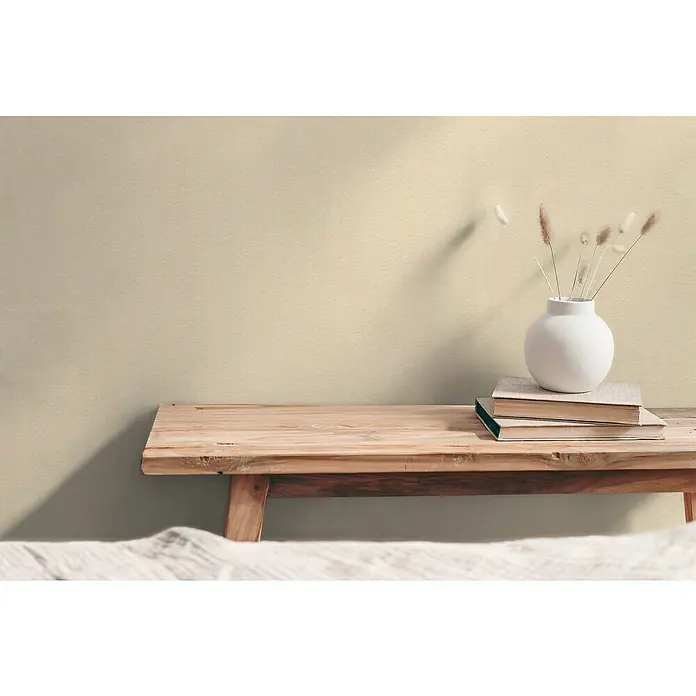 A.S. Création Hygge 3 Vliestapete - Beigecreme, Uni, 10,05 x 0,53 m - Stillleben mit einem Stapel Bücher und einer Vase mit Trockenblumen auf einem Holztisch vor einer beigen Wand.