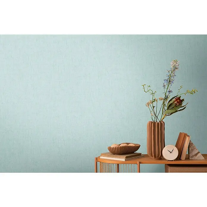 A.S. Création Cosmoliving by Cosmopolitan Vliestapete - Helles Blau, Uni, 10,05 x 0,53 m - Nahaufnahme eines dekorierten Tisches mit einer braunen Vase, einer Schale, Büchern und einer Uhr, vor einer mintgrünen Wand.
