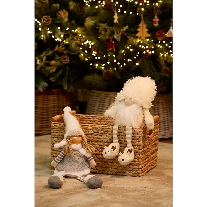 Figura decorativa Lapua - Textil - Dos adorables muñecas de peluche sentadas en una cesta de mimbre frente a un árbol de Navidad festivo y parpadeante.