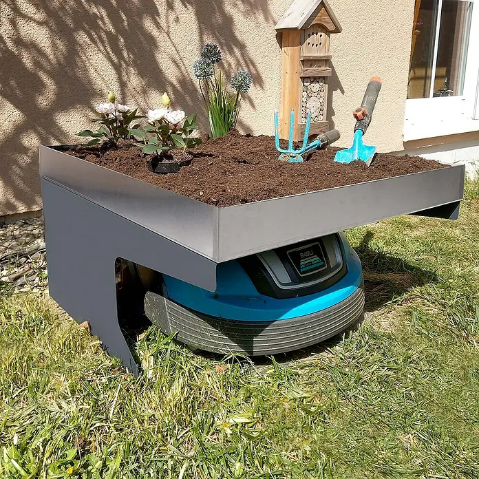 Proregal Mähroboter-Garage Mähroboter-Garage mit Pflanzkasten - Edelstahl-Anthrazit - Ein Rasenmähroboter mit einem aufgesetzten Blumenkasten, bepflanzt mit Blumen und Gartenwerkzeugen im Garten.