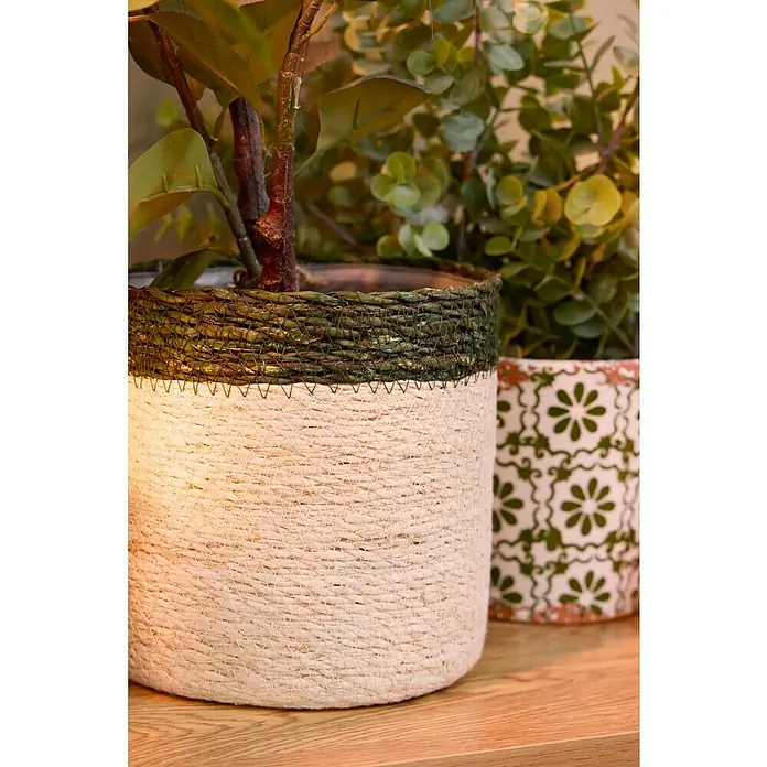 Maceta con interior de plástico Eli - Ø x Al: 14 x 14 cm, Natural, Crema/Verde - Maceta decorativa, tejida, con un borde verde y una parte inferior de color claro, junto a otra maceta con estampado floral.