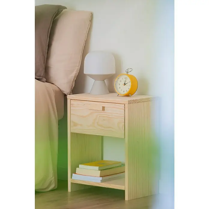 Astigarraga Vita Conjunto de muebles - Natural, 4 pzs. - Esta imagen muestra una mesita de noche de madera clara con un cajón, una lámpara y un despertador amarillo encima, con libros en el estante inferior.