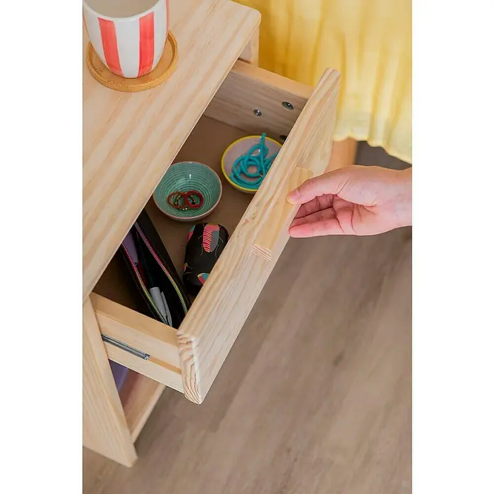 Astigarraga Vita Mesita de noche - L x An x Al: 25 x 40 x 50 cm, Natural, Número de cajones: 1 ud. - Primer plano de una mesa de madera abierta con una taza y varios objetos dentro de un cajón que está abriendo una mano.