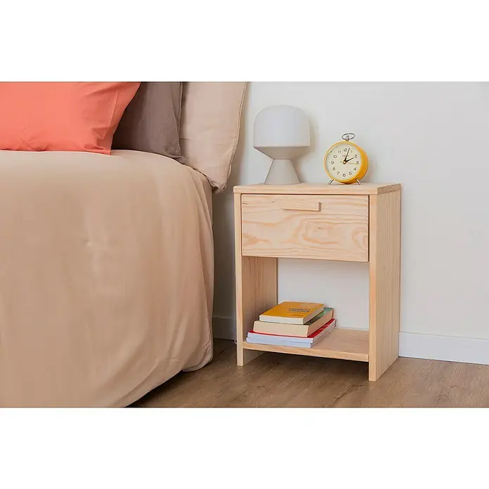 Astigarraga Vita Conjunto de muebles - Natural, 4 pzs. - Mesita de noche de madera con cajón, lámpara y despertador, junto a una cama con cojines de colores, ofreciendo almacenamiento práctico y diseño elegante.