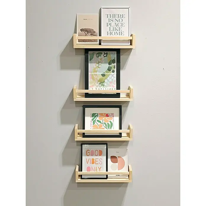Astigarraga Especiero - L x An x Al: 15 x 40 x 15 cm, Madera, Natural - Estantes de madera clara con borde para cuadros adornan una pared gris, mostrando obras de arte enmarcadas y creando un arreglo decorativo.