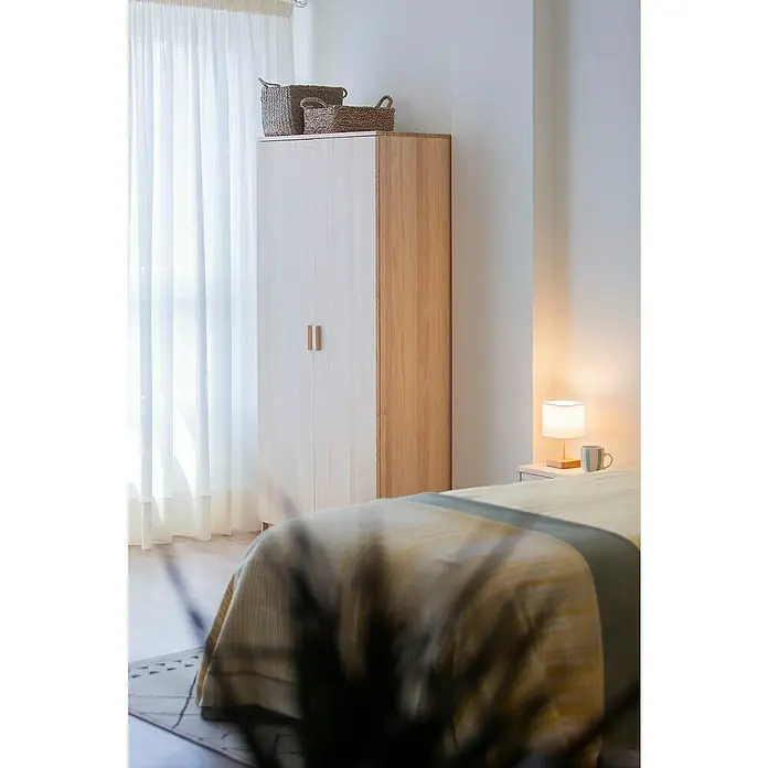 Astigarraga Vita Conjunto de muebles - Natural, 4 pzs. - Un espacioso armario hecho de madera clara y blanco está en una habitación luminosa, con dos cestas colocadas encima.