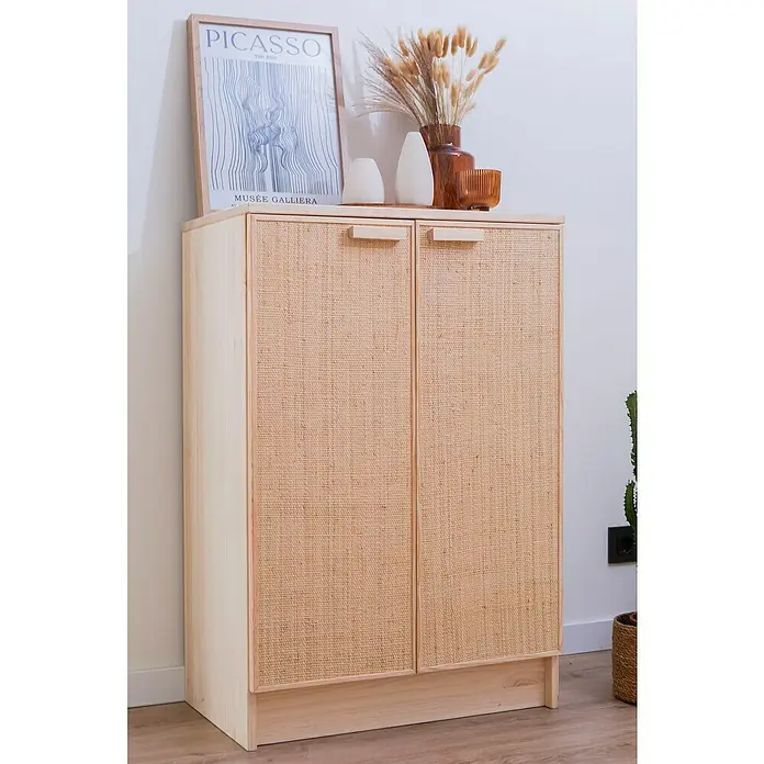 Astigarraga Aura Conjunto de muebles - 2 pzs., Madera maciza y rafia, Natural - La foto muestra un armario de madera con dos puertas y tiradores. En la parte superior, hay decoraciones y un póster de Picasso enmarcado.