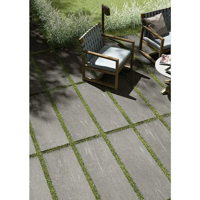 Esterno 20 T by Palazzo Terrassenfliese Davos40 x 120 x 2 cm, Greige, Matt - Eine Nahaufnahme von grauen Terrassenplatten mit Grasfugen, die einen modernen und natürlichen Außenbereich schaffen.