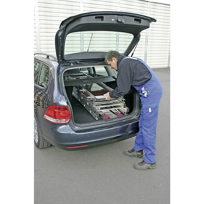 Krause Corda Gelenkgerüst - Arbeitshöhe: 5 m, Belastbarkeit Plattform: 135 kg, Breite Plattform: 0,56 m, Länge Plattform: 1,5 m - Mann verlädt eine Aluminium-Mehrzweckleiter in den Kofferraum eines Autos. Die Leiter ist zusammengeklappt und liegt im Kofferraum.
