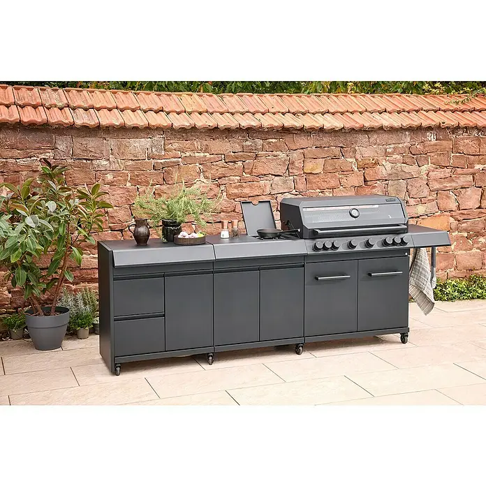 Kingstone Outdoorküchen-Modul Cliff Big Basic - Schwarz, B x T x H: 82 x 55,5 x 91 cm - Ein grauer Außenküchengrill mit Ablageflächen und Schränken vor einer Ziegelmauer, umgeben von Grünpflanzen, bietet viel Platz.