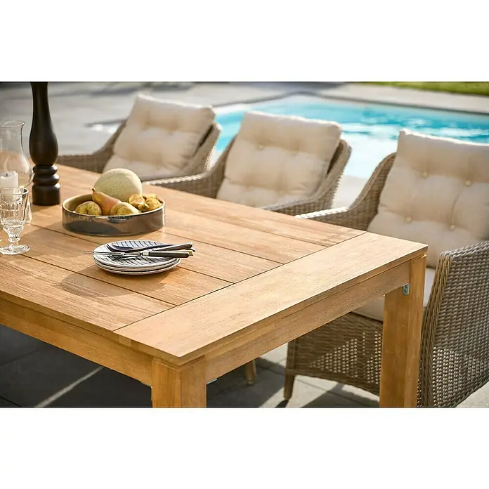 Sunfun Laura Gartentisch - L x B x H: 220 x 100 x 76 cm, Akazie, Rechteckig, Naturbraun - Ein Teakholztisch ist mit Tellern, Besteck, Obst und Gläsern dekoriert, umgeben von Korbstühlen und mit einem Pool im Hintergrund.