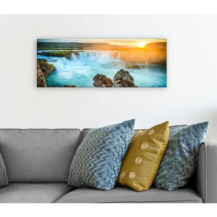 Glasbild - Colourful Waterfall, B x H: 80 x 30 cm - Ein Wandbild von einem Wasserfall hängt über einem grauen Sofa mit Kissen. Das Landschaftsbild bringt die Natur in Ihr Wohnzimmer.