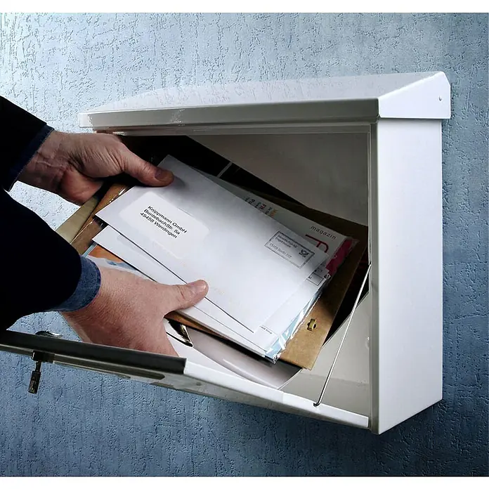Proregal Wandbriefkasten Comfort aus verzinkem Edelstahl - Weiß, Stahl - Blick in einen Briefkasten mit Post, der an einer blau gestrichenen Wand montiert ist. Eine Hand nimmt Post entgegen.
