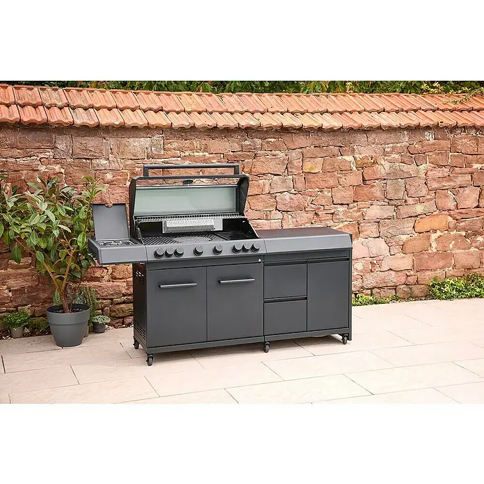 Kingstone Outdoorküchen-Modul Cliff Big Basic - Schwarz, B x T x H: 82 x 55,5 x 91 cm - Ein grauer Grill mit mehreren Brennern und Schränken steht auf einer Terrasse vor einer roten Ziegelmauer.