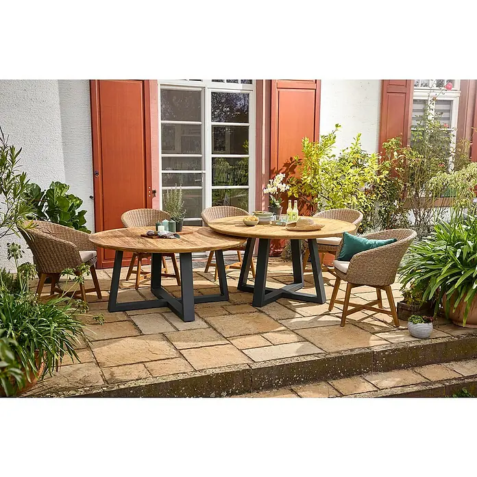 Sunfun Tischbein-Set Low-Dining - für Tischplatte ⌀ 150 cm, Höhe: 65 cm, Aluminium, Anthrazit - Eine Gartenszene mit zwei runden Holztischen auf dunklen Metallfüßen, umgeben von Korbstühlen und üppigem Grün.