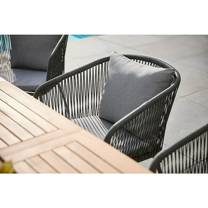 Sunfun Maja Gartensessel - Kunststofffaser-Strings, Grau, B x T x H: 62 x 62 x 78 cm - Nahaufnahme von modernen grauen Rattanstühlen mit Kissen, die um einen Holztisch im Freien angeordnet sind.