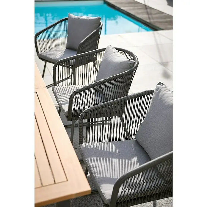 Sunfun Maja Gartensessel - Kunststofffaser-Strings, Grau, B x T x H: 62 x 62 x 78 cm - Drei graue Rattan-Sessel mit bequemen Kissen stehen neben einem Swimmingpool und laden zum Entspannen im Freien ein.