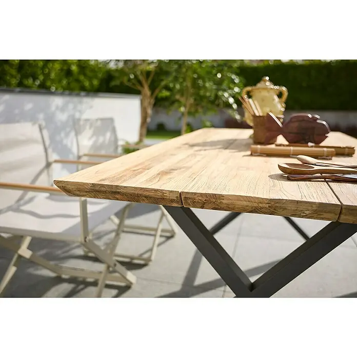 Sunfun Garten-Tischplatte - L x B: 180 x 90 cm, Teak, Schweizer Kante - Nahaufnahme eines rechteckigen Holztisches mit Dekorationsgegenständen und Stühlen im Hintergrund.