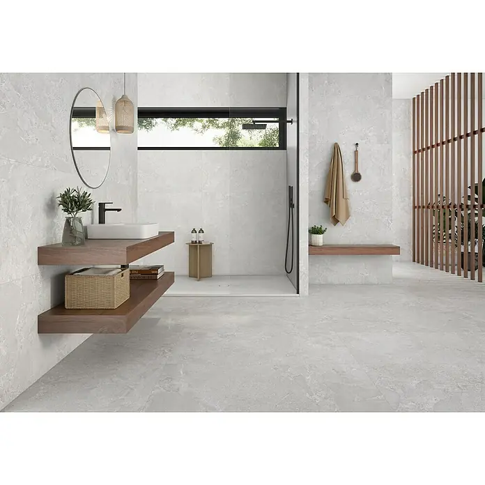 Pavimento porcelánico Avalon Rock - 60 x 60 cm, Blanco, C-3 Antideslizante, Mate - Un baño moderno con azulejos grises, estantería de pared de madera y ducha a ras de suelo para un espacio elegante y sereno.