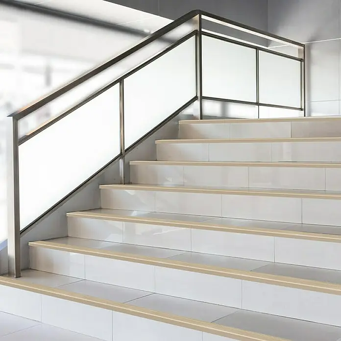 Floordirekt Treppenkantenprofil Safety 90 cm Gold - Aluminium, Gold, Eloxiert - Nahaufnahme einer Treppe mit Stufenkantenprofilen und einem Geländer aus Glas und Metall, das für Sicherheit und ein modernes Design sorgt.