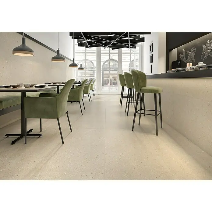 Pavimento porcelánico Avalon Rock - 60 x 60 cm, Arena, C-3 Antideslizante, Mate - Interior de un restaurante con suelo de terrazo, sillas verde oliva y lámparas colgantes.