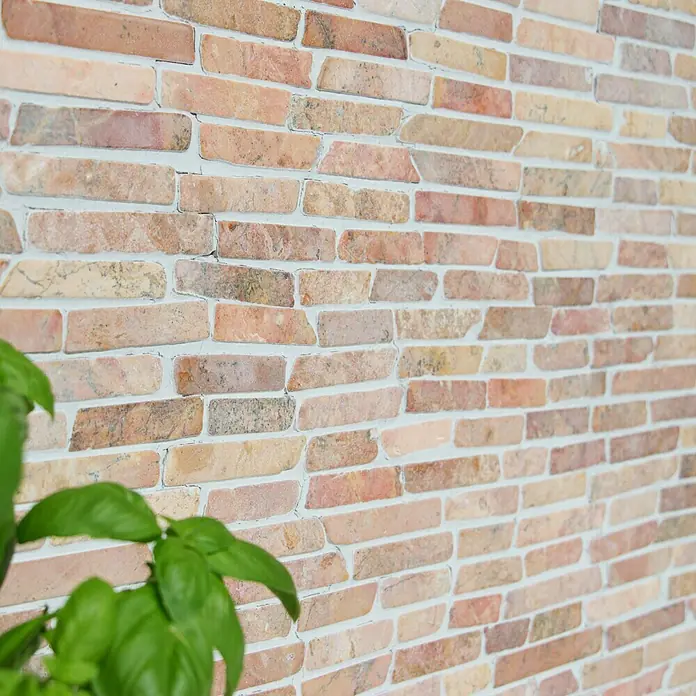 Mosaikfliese MOS BRICK 145 - 30,5 x 30,5 cm, Rot, Matt - Nahaufnahme einer dekorativen Wand mit auffälligen, länglichen Ziegeln in verschiedenen Rot- und Beigetönen, die ein rustikales Ambiente schaffen.