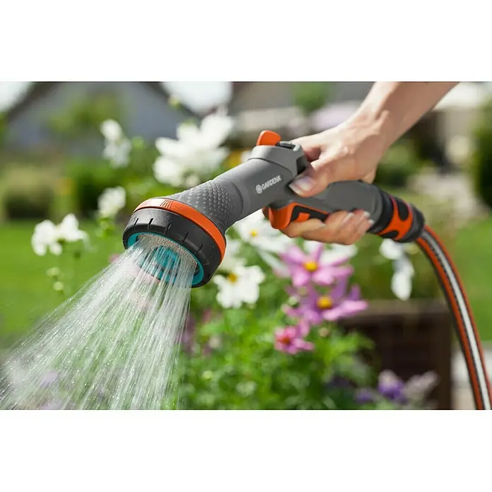 Gardena Comfort Brause - Anzahl Sprühformen: 2 Stk., Metall/Kunststoff - Nahaufnahme einer Hand, die einen Gardena-Gartenschlauch mit Wassersprühkopf hält, der Wasser auf Blumen sprüht.