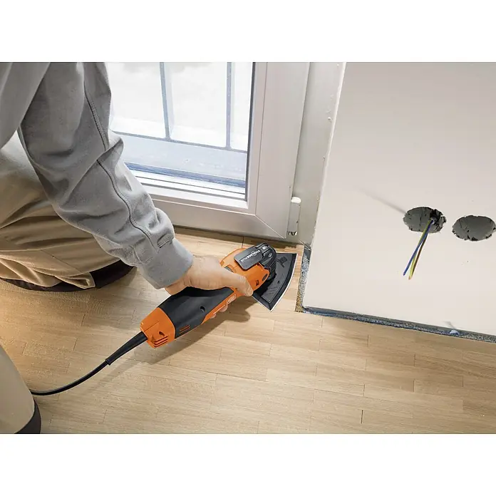 Fein Starlock Plus Schleifblatt-Set - 7 Stk., 7 -tlg., Körnung: 60 mm - 80 mm - Ein Handwerker benutzt ein FEIN Oszillierer, um Holzarbeiten an einem Fensterrahmen durchzuführen. Das Elektrowerkzeug ist orange und schwarz.